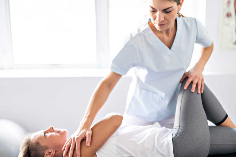 Chiropractor and physical therapist reviewing movement exercises with an adult patient in a bright treatment room