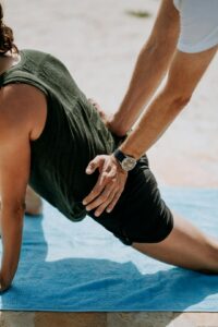 Adult performing gentle back exercises beside a treatment table while reviewing posture and movement with a practitioner.