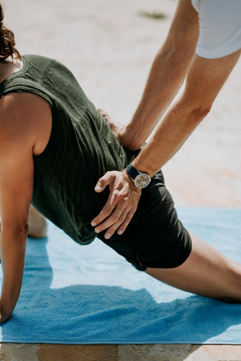 Adult performing gentle back exercises beside a treatment table while reviewing posture and movement with a practitioner.